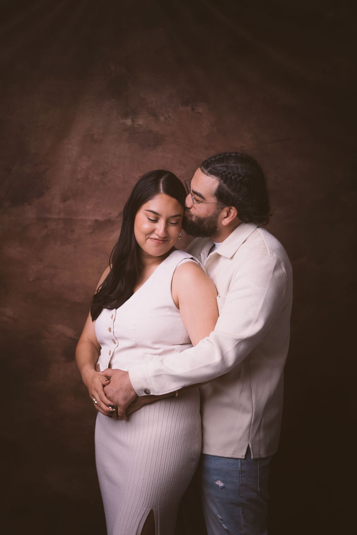 An intimate portrait showing a tender moment between a couple against a dark brown backdrop.