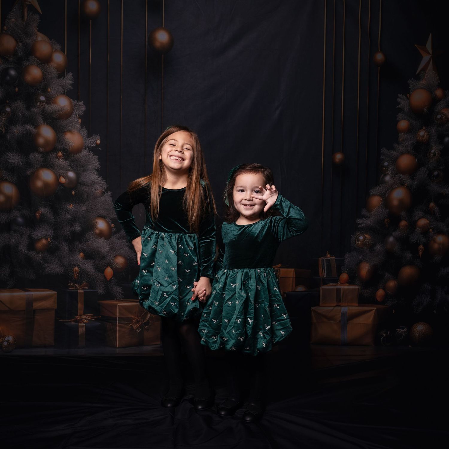 Studio portrait session with emerald green velvet dresses against dark backdrop.