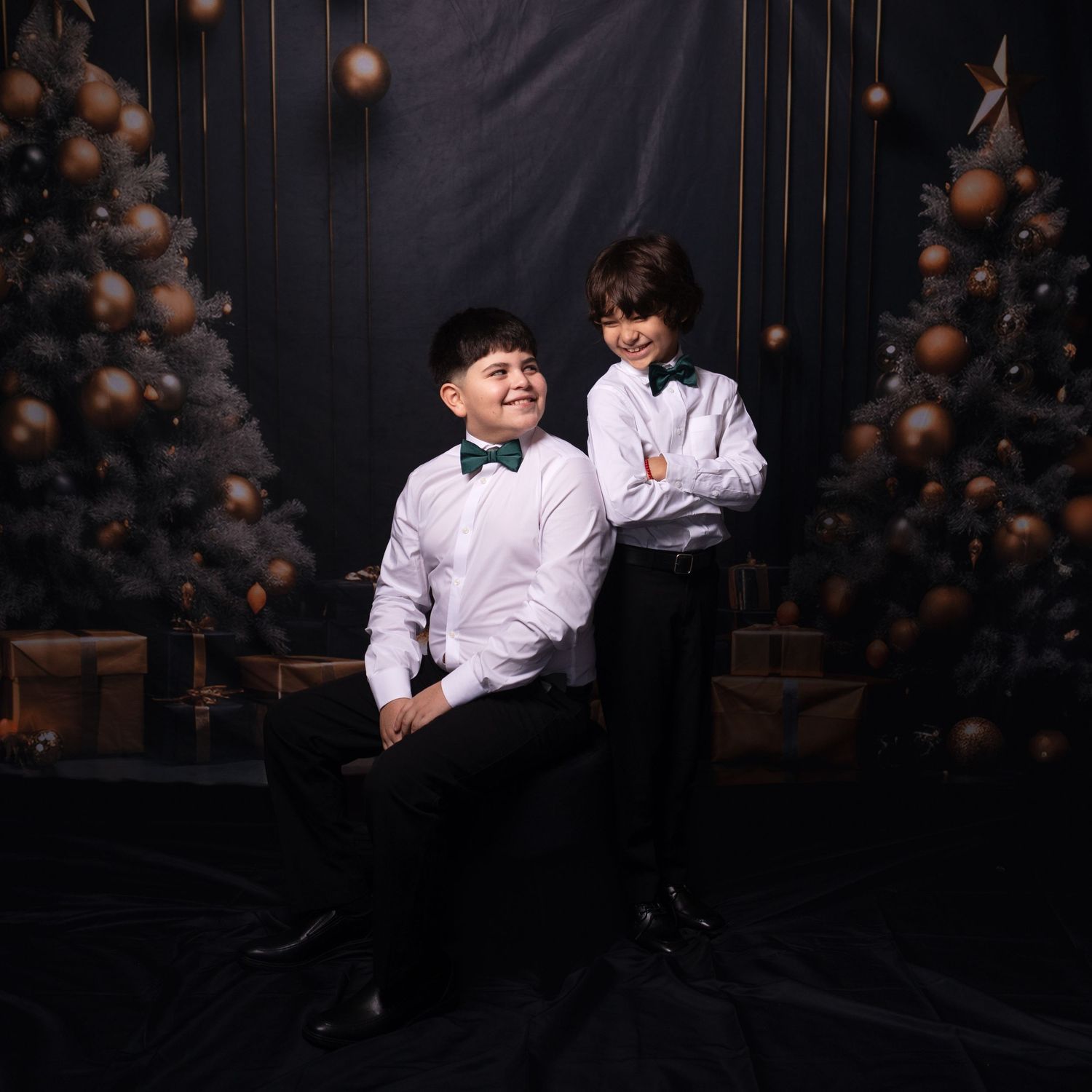 Siblings in formal wear posing during dark studio photography session.