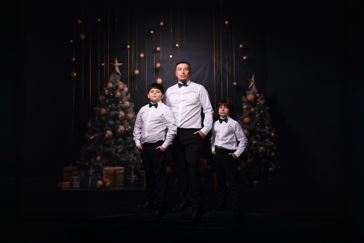 Two people in formal wear smile together against a dark backdrop with hanging ornaments.