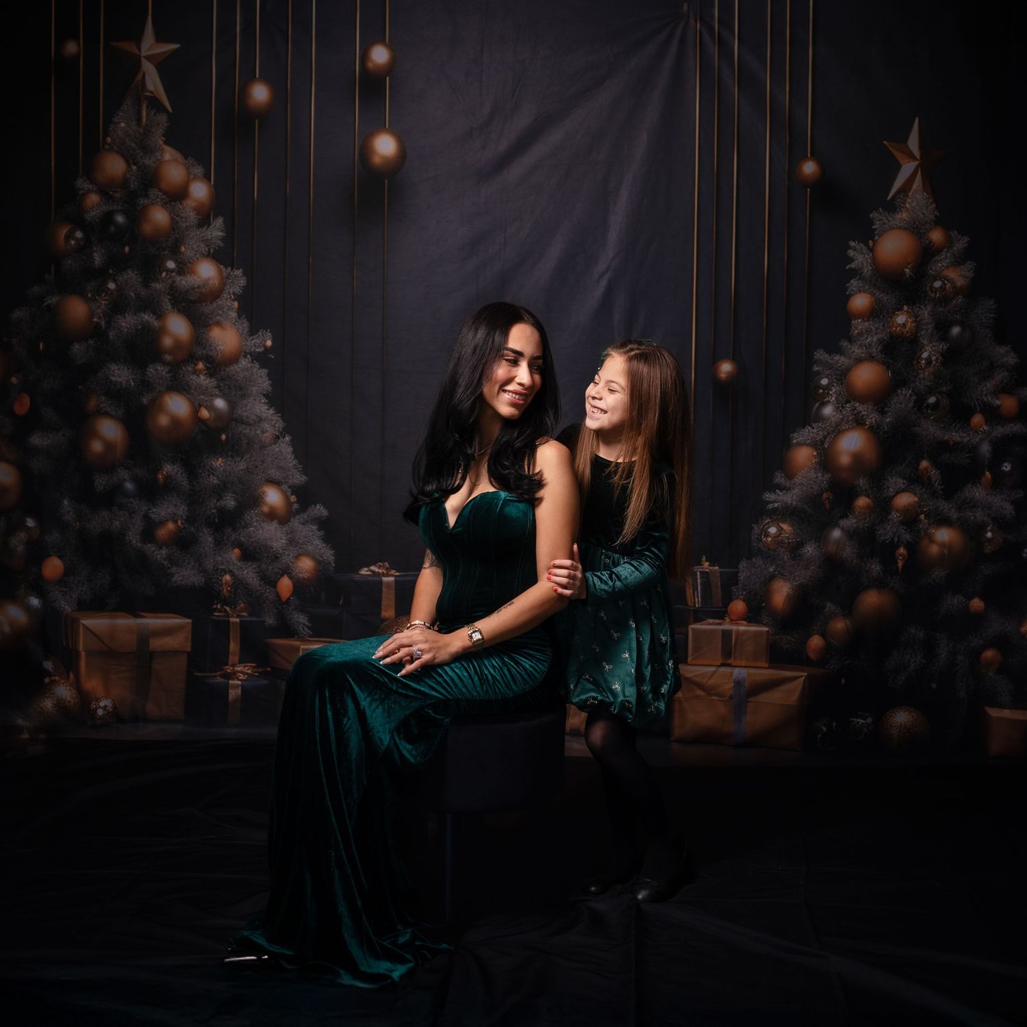 Two people in elegant green dresses pose on dark floor with decorative backdrop.