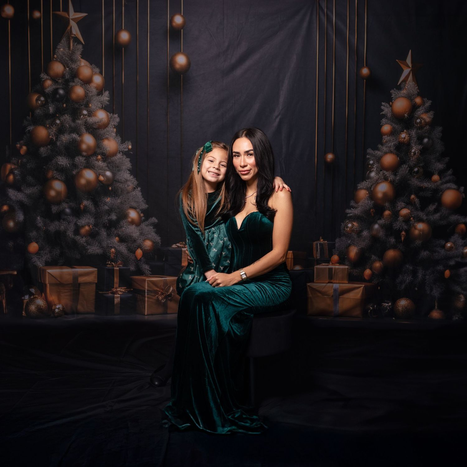 Two people wearing emerald velvet dresses share a joyful moment against dark holiday decor.