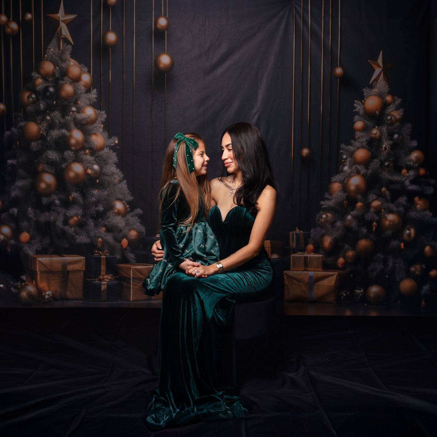 Two people in matching green velvet dresses pose elegantly against festive backdrop.