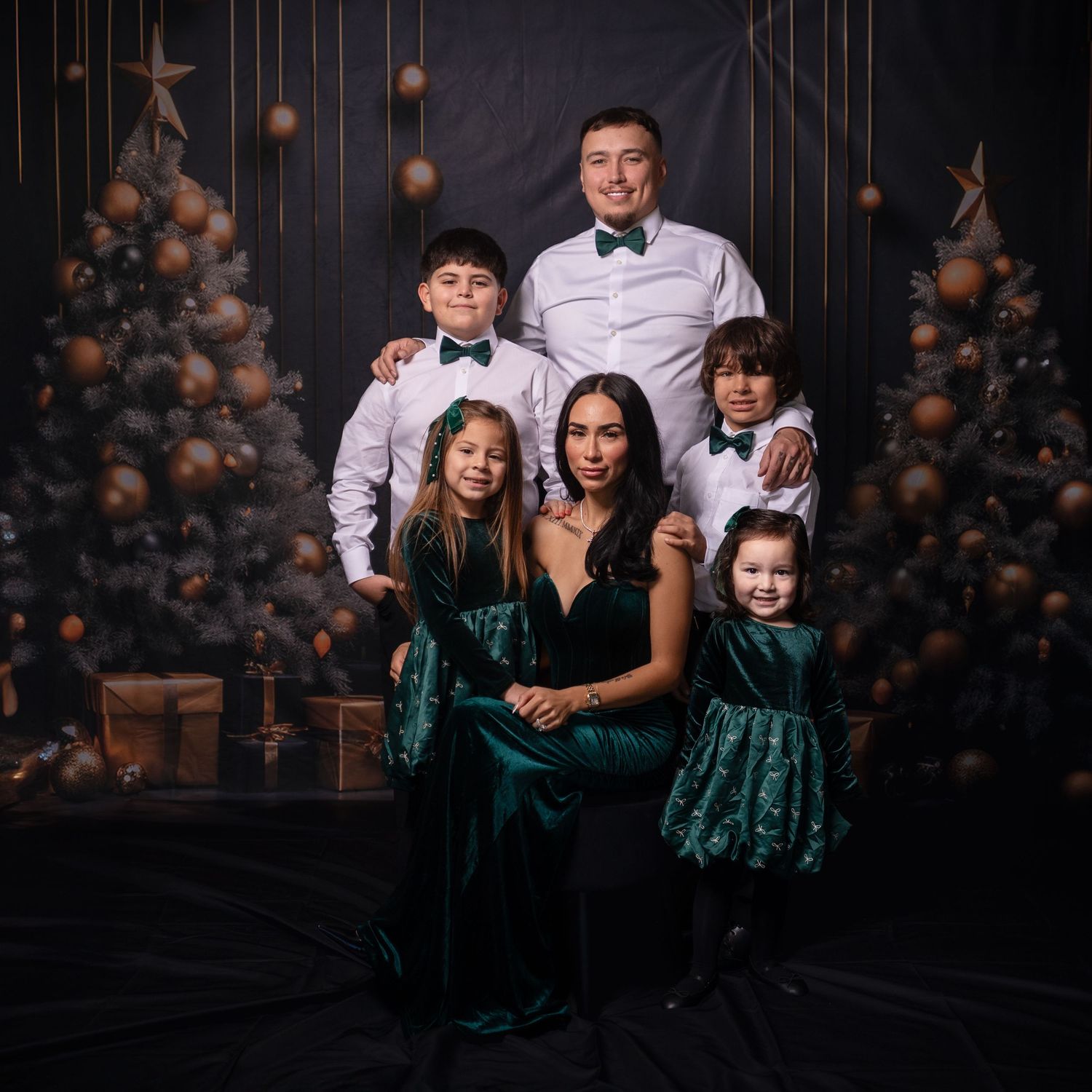 Family portrait with matching formal attire against dark backdrop with hanging ornaments.