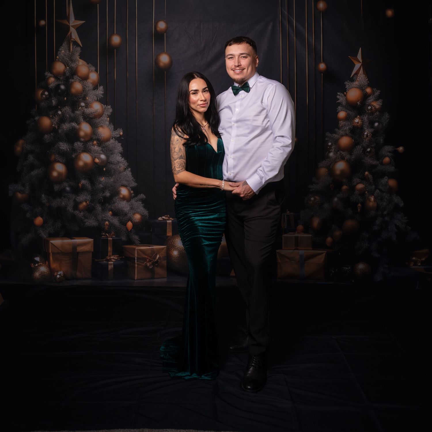 Stylish couple in black and white attire embraces in studio with holiday decorations.