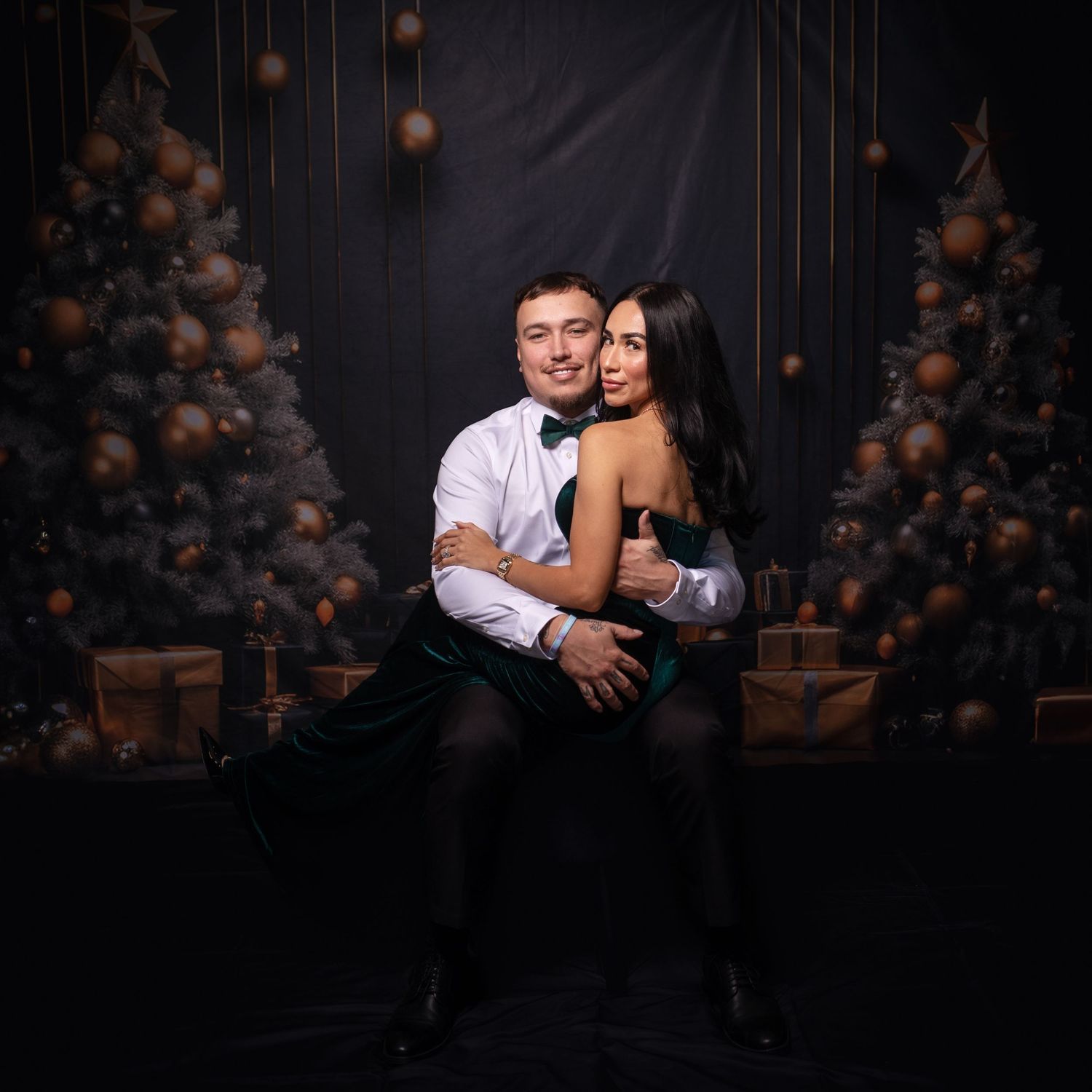 Intimate portrait session with couple in formal wear against dark festive backdrop.