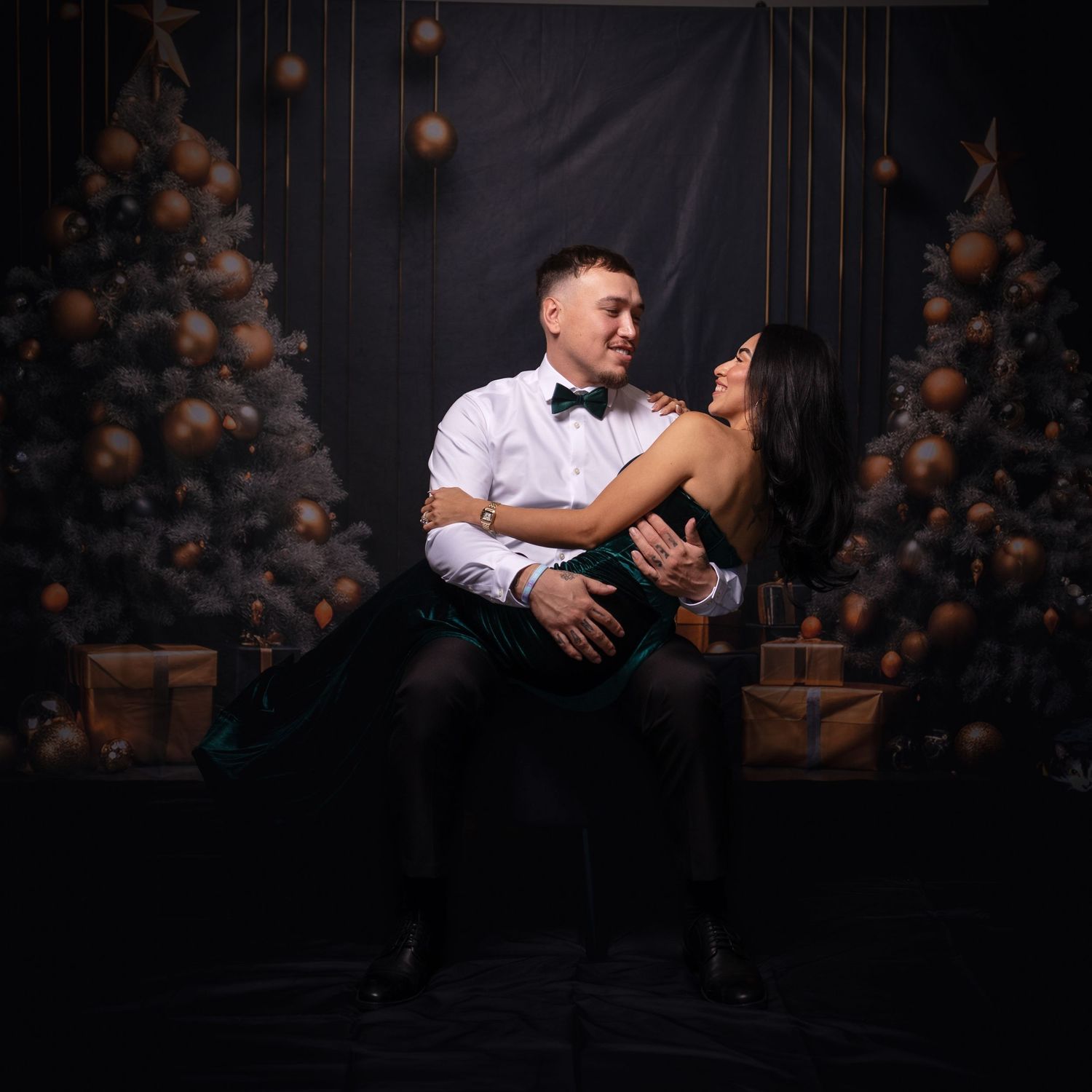 Dramatic studio portrait of couple in formal wear against dark holiday setting.