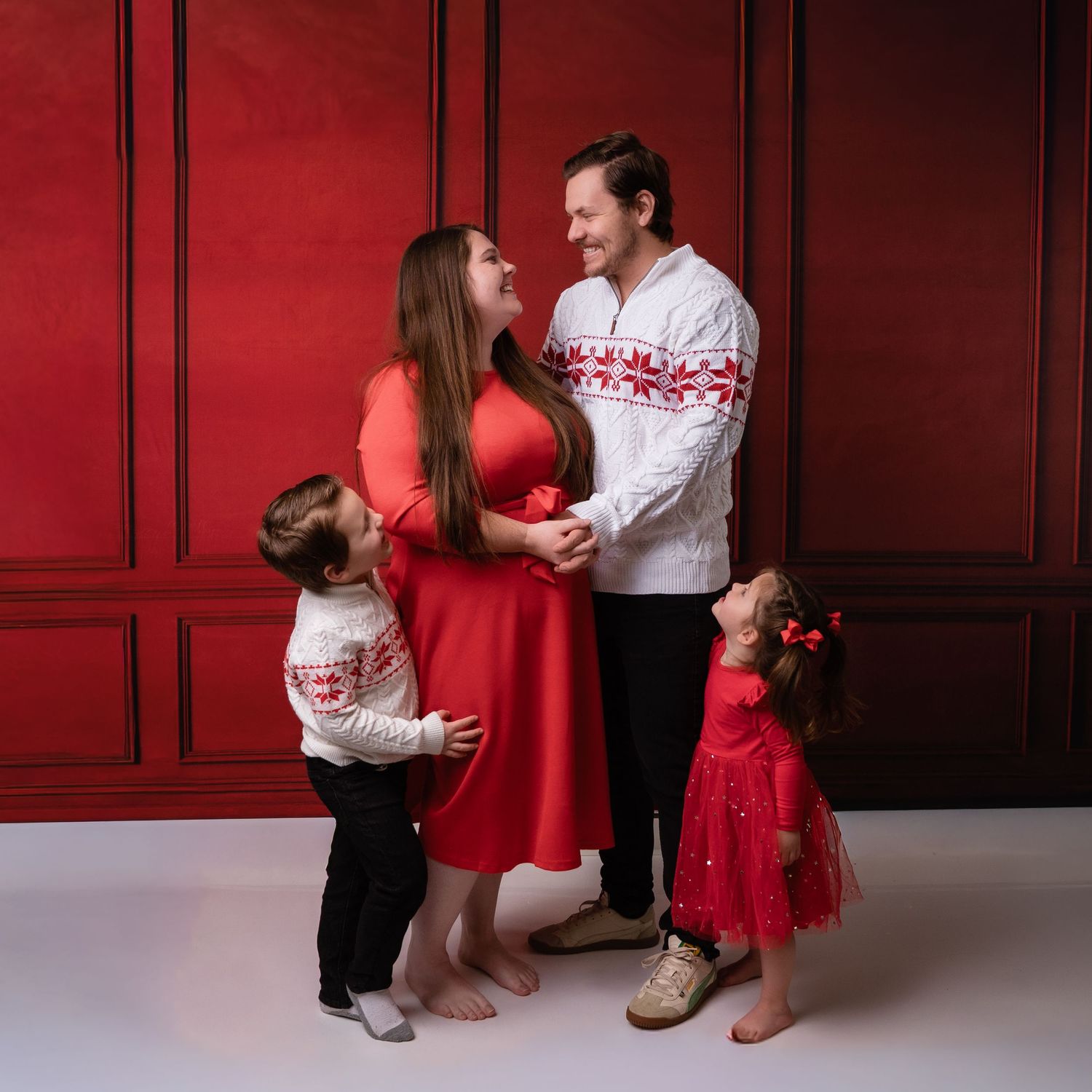 Candid family moments captured against red wall in festive holiday attire.