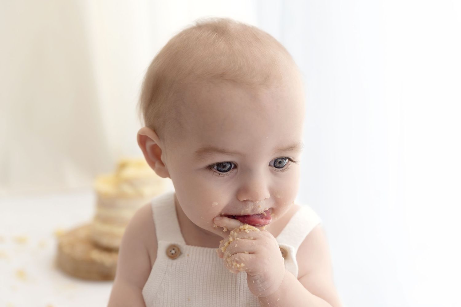 A young child in white overalls enjoys eating a chocolate cookie with a messy face.