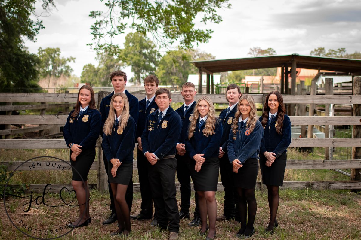 A group in matching navy jackets poses together outdoors by wooden fences at a rustic venue.