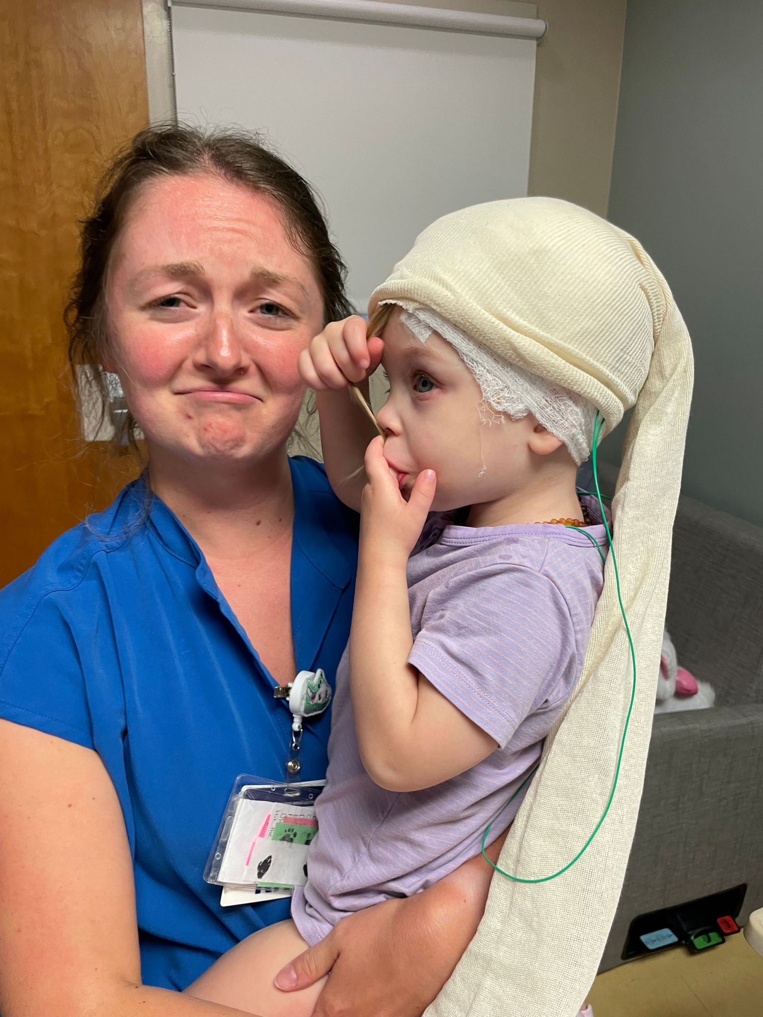 A caring interaction between a medical professional in blue scrubs and a young patient wearing a soft head covering.