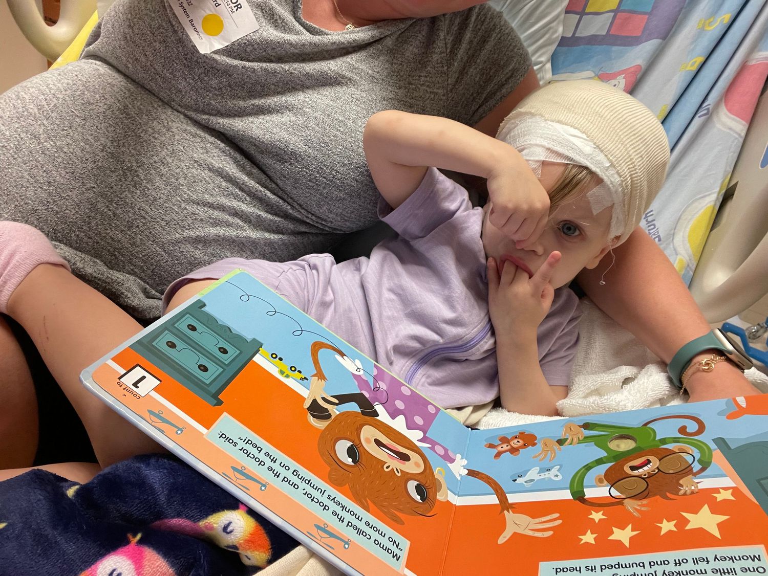 A small child reading a colorful storybook with illustrations while lying down.
