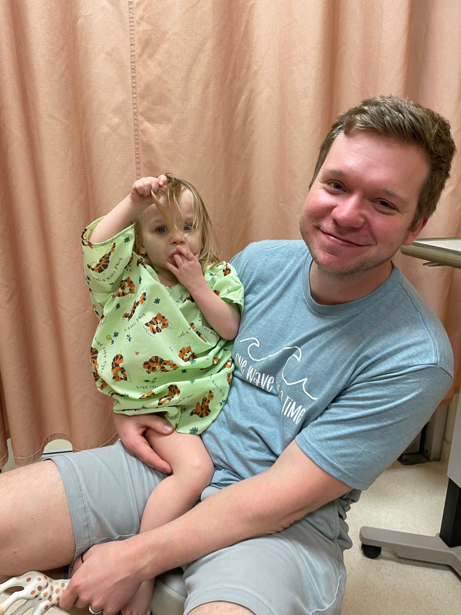 An adult and a toddler in a green animal print outfit sitting together in a medical exam room.