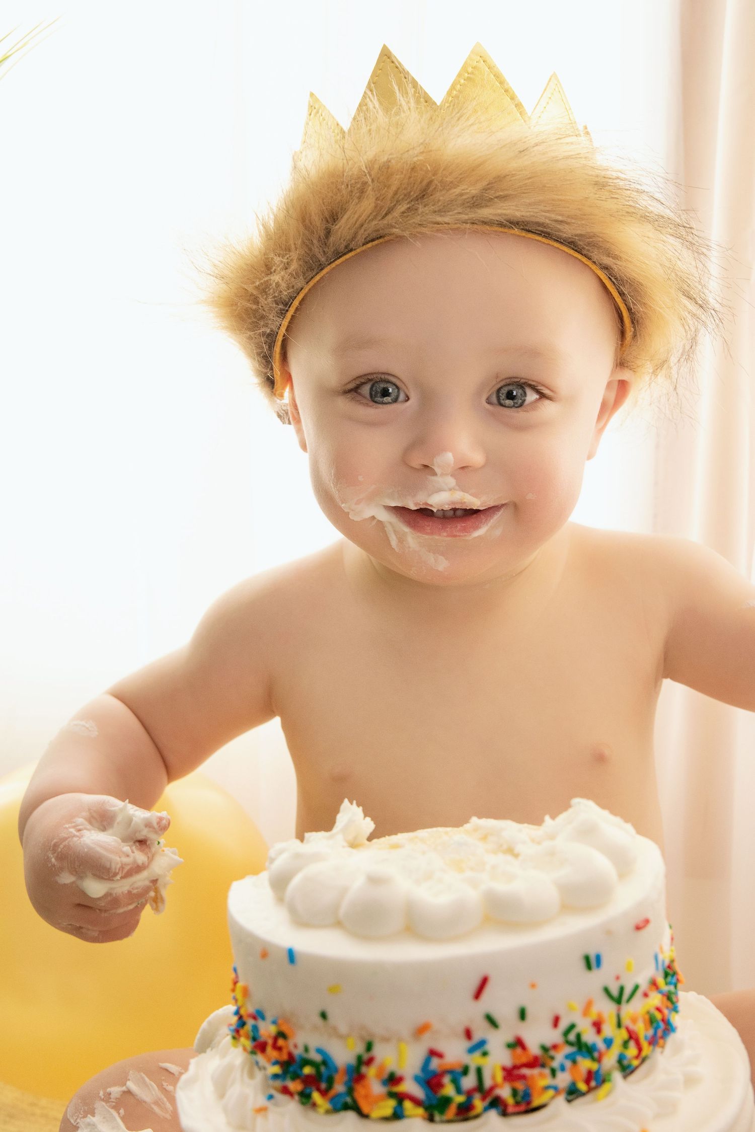 child wearing a lion hat during a cake smash session, covered in cake and joy.