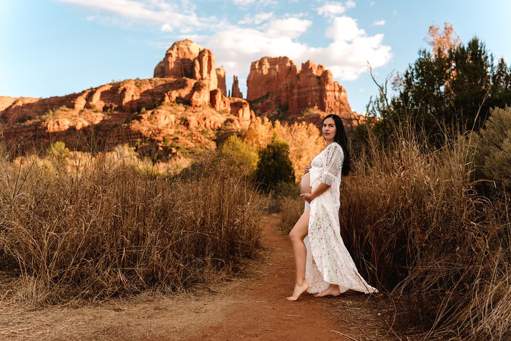 Ethereal maternity photo with white dress against Sedona red rock formations in desert landscape.