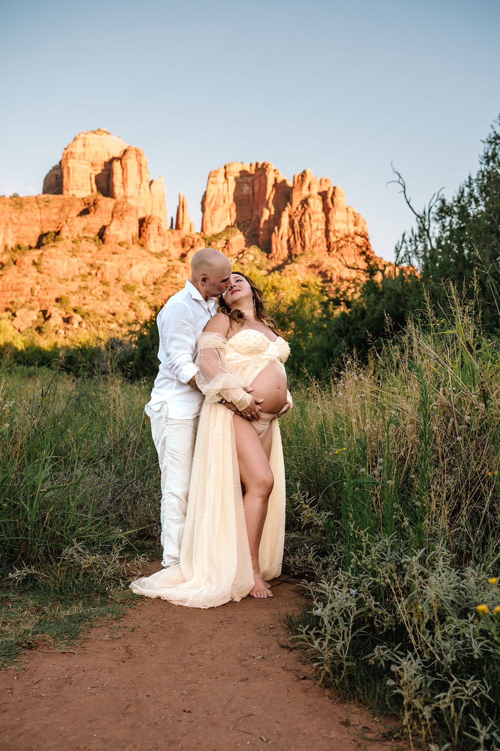 Couple embracing in Sedona with Cathedral Rock backdrop during golden hour maternity session.