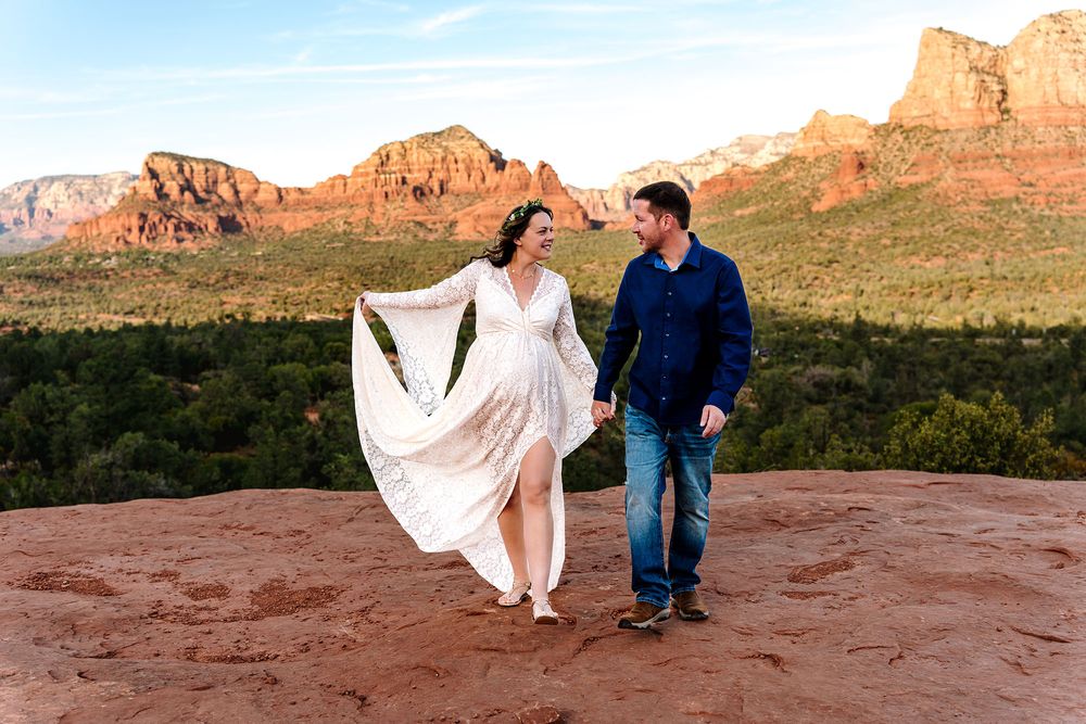Couple holding hands in white dress and jeans with red rock Sedona Arizona landscape at sunset.