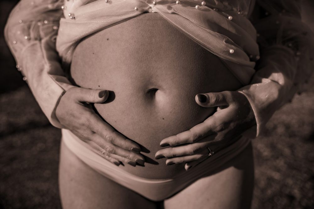 Black and white artistic photo of hands forming a heart shape on a pregnant belly.
