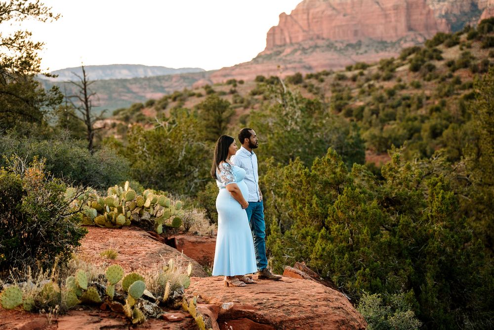 Couple standing on red rocks in Sedona Arizona surrounded by cacti and red rock formations at sunset.