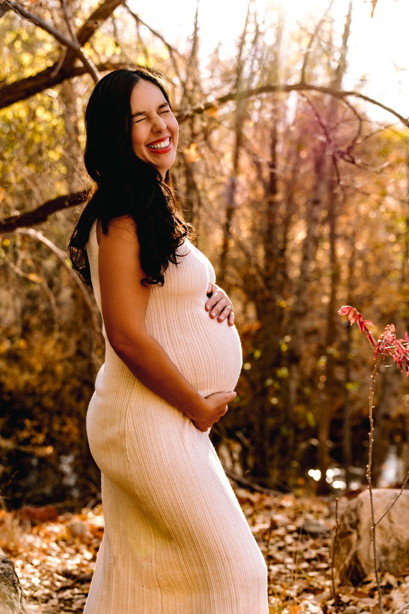 Joyful maternity portrait in cream dress surrounded by fall foliage.