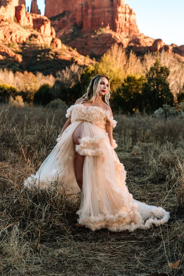 Elegant flowing champagne gown with ruffled details photographed against dramatic red rock formations at sunset.