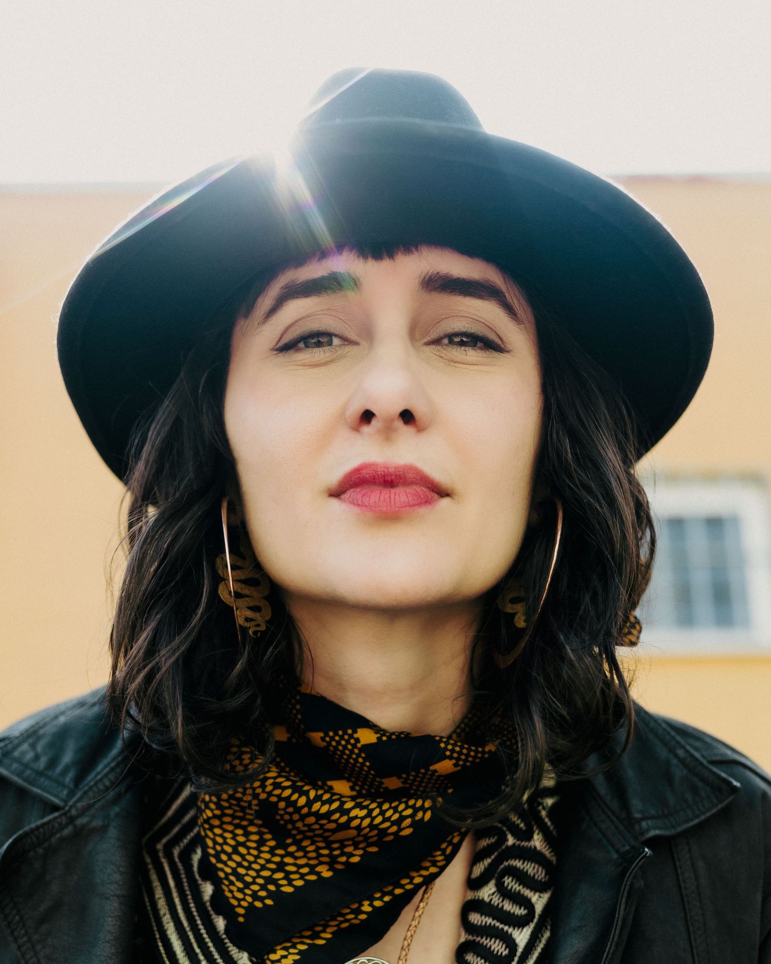 A person wearing a black hat and scarf poses stylishly against a light background in a fashion portrait.