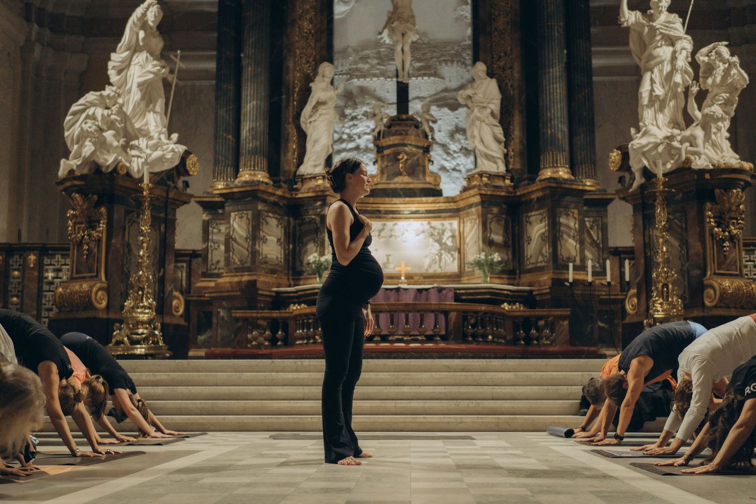 a pregnant yoga teacher looking over group of people standing in yoga poses while being captured by event photographer in Stockholm