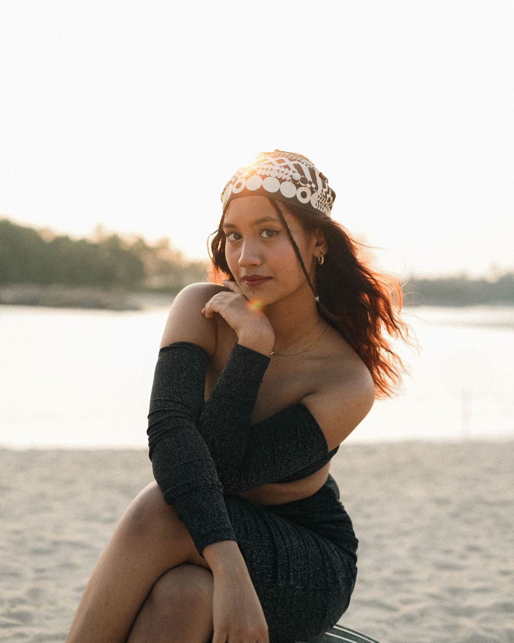 Sunset beach portrait in black off-shoulder outfit with patterned headpiece and natural lighting.