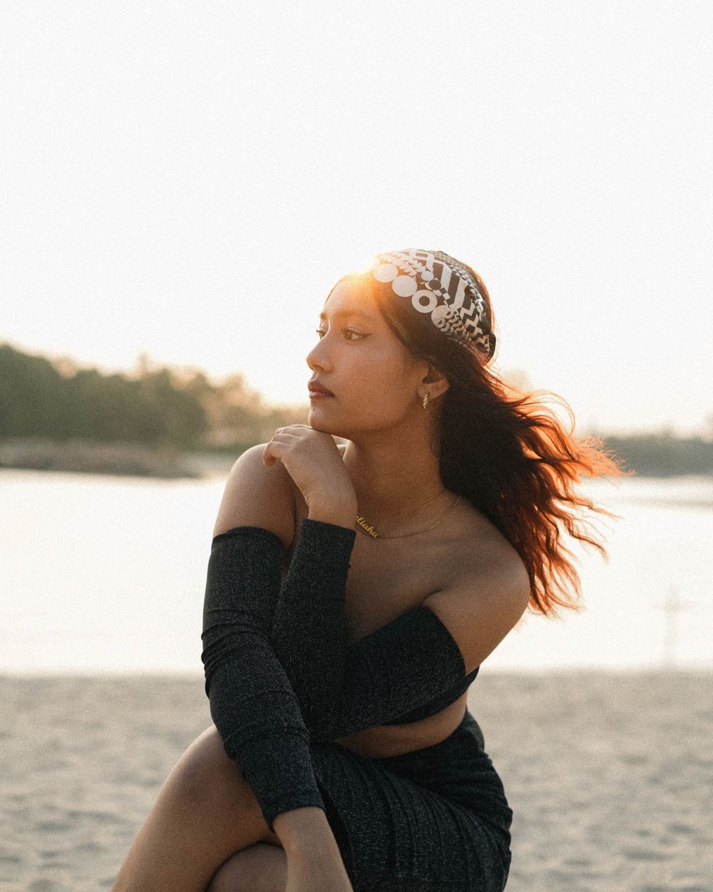 Side profile beach photo with wind-swept hair, black outfit and patterned headwear at golden hour.