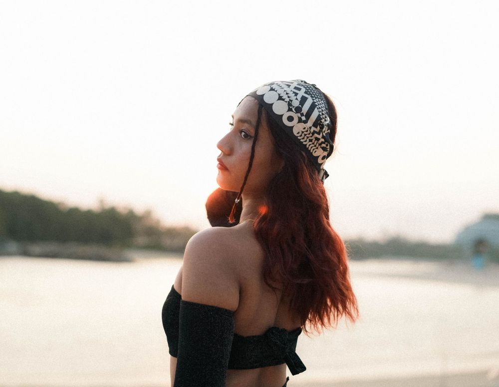 Beachside fashion portrait featuring black off-shoulder top and patterned headpiece during sunset.