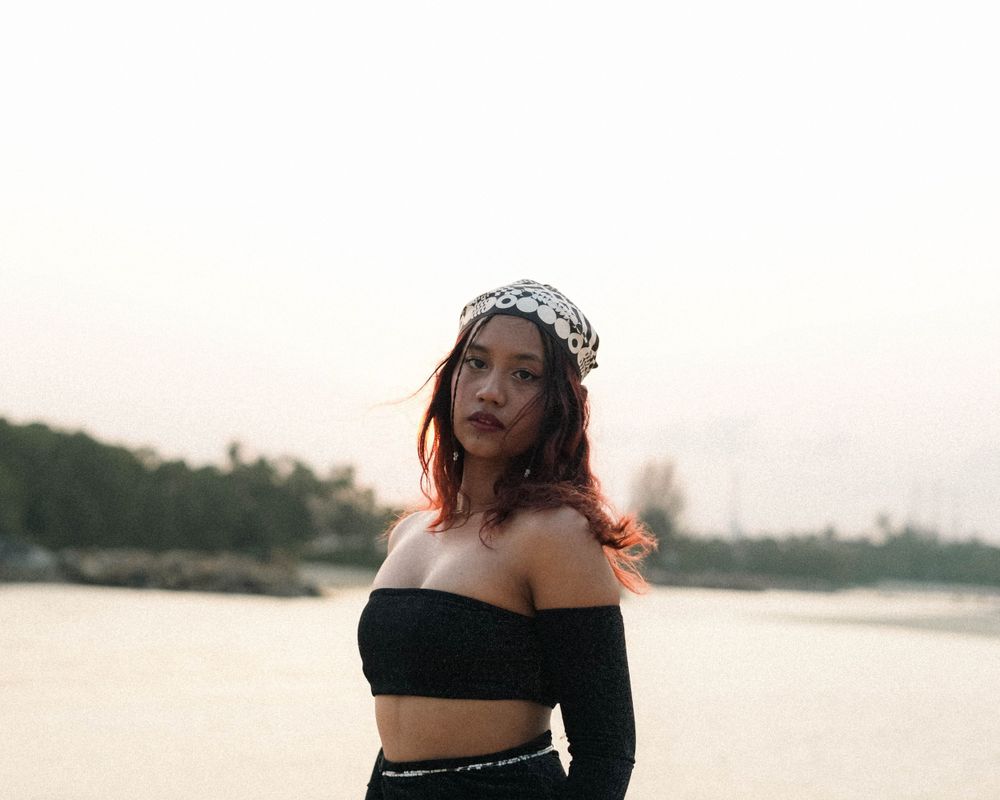 Seaside portrait in black off-shoulder ensemble and decorative headpiece during golden hour.