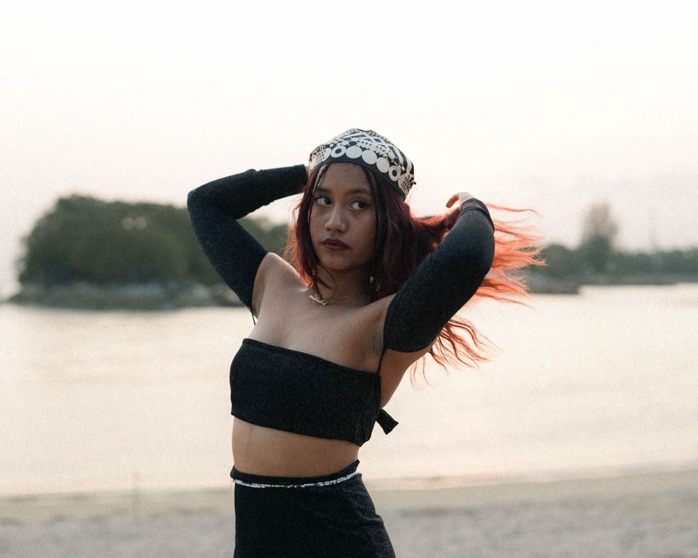 Fashion pose with flowing hair in black crop top and patterned headpiece by the water.