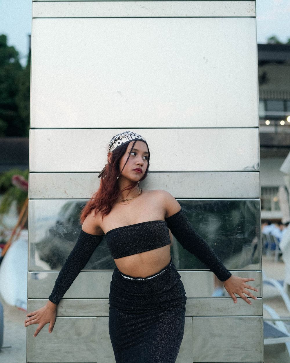 Modern fashion pose against white wall wearing black crop top ensemble and patterned headpiece.
