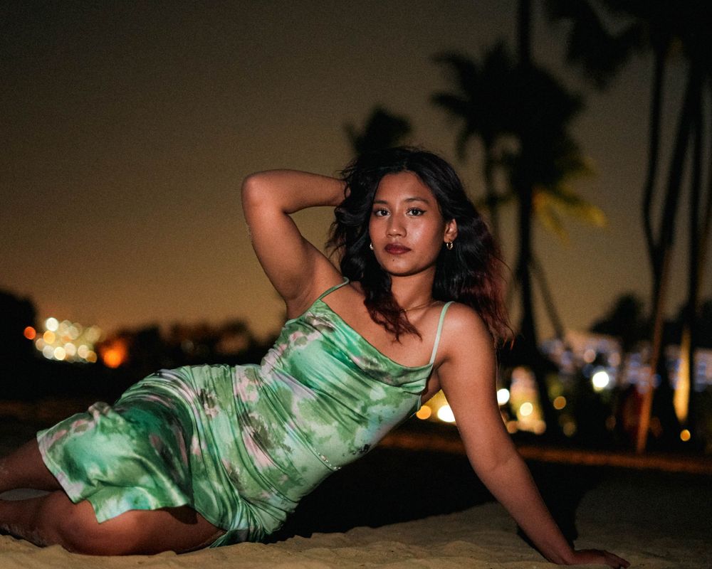 Artistic nighttime portrait in green tie-dye dress with palm trees and city lights backdrop.