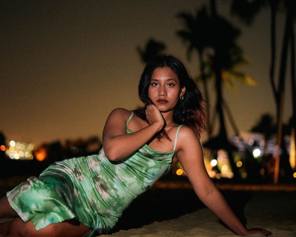 A sea green dress creates a tropical evening silhouette against a palm-lined beach at sunset.