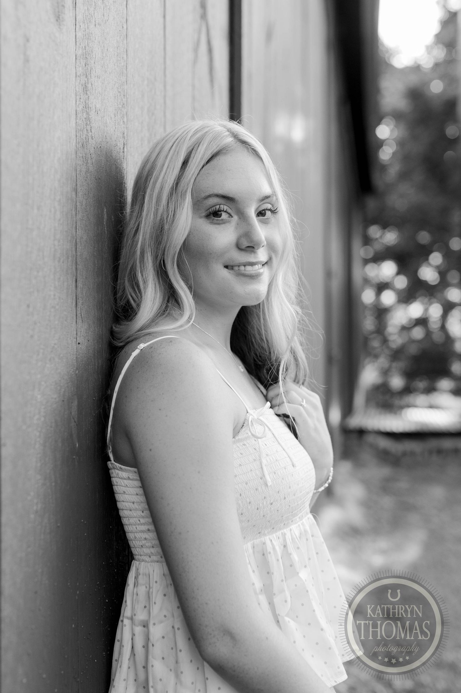 Black and white portrait against wooden wall wearing white summer dress with natural lighting.