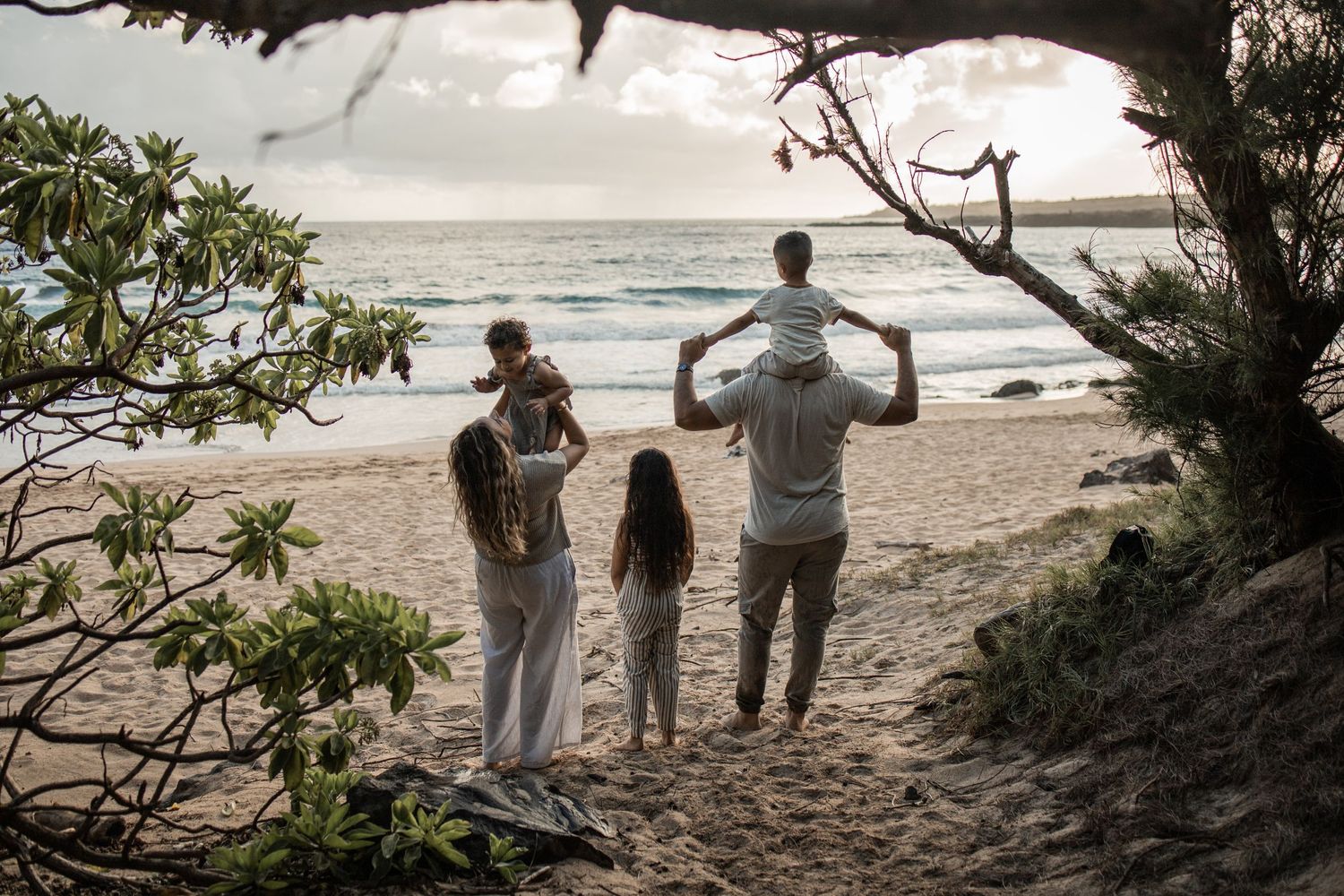 The backs of family of five standing on Maui beach looking toward the ocean