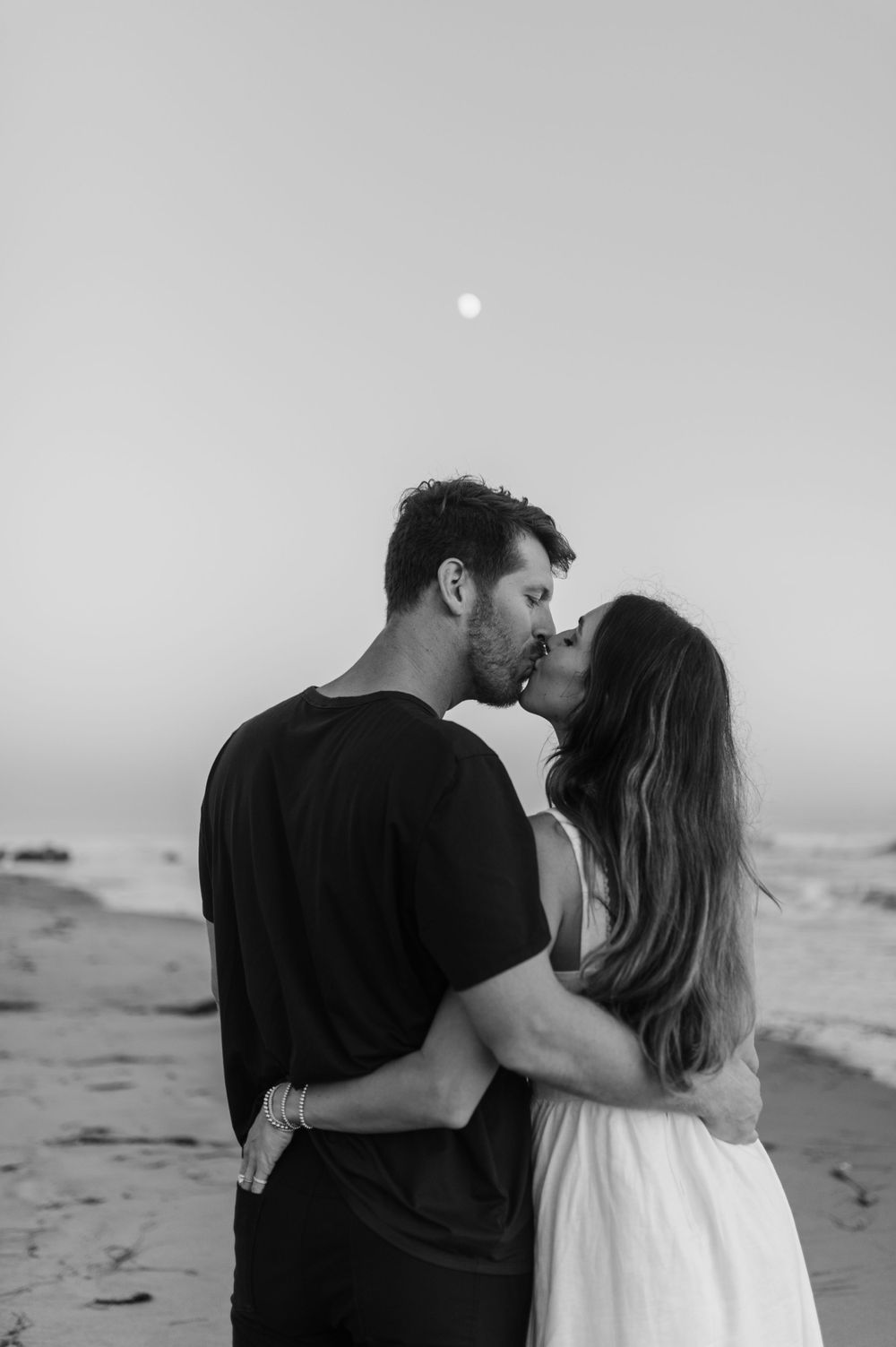 A romantic black and white photograph of a couple sharing an intimate moment on the beach.