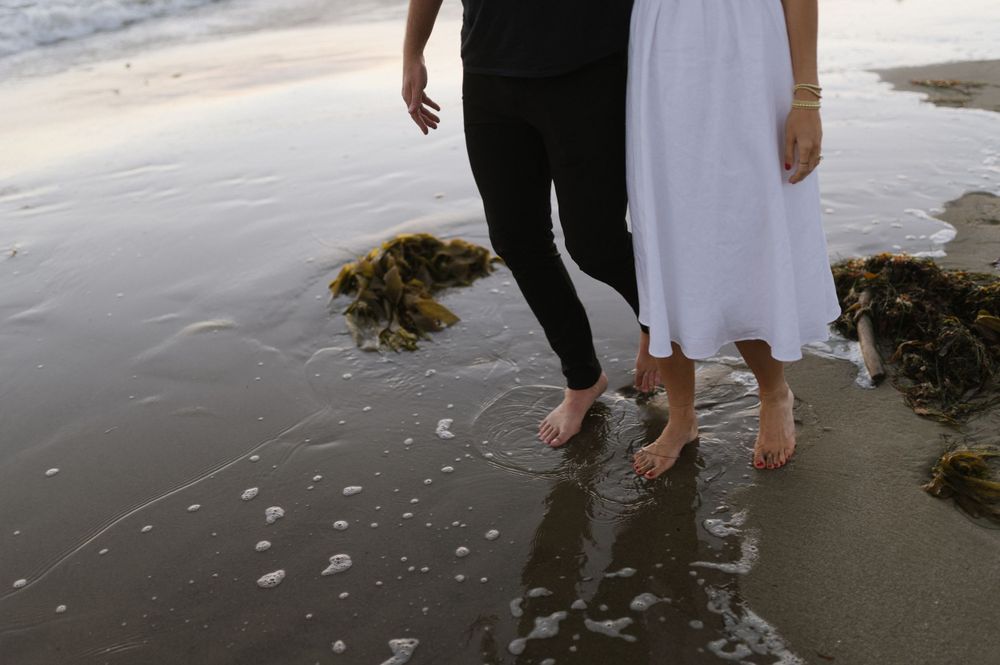 Close-up of feet standing in shallow ocean water on a sandy beach.