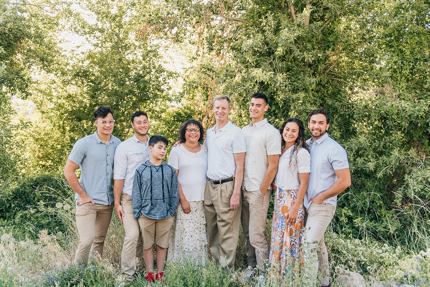 A group in coordinated light blue and khaki outfits pose together outdoors in a natural sunlit setting.