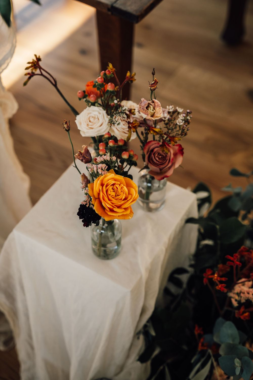 Close-up of orange and pink roses in mason jar arrangements on white linens.