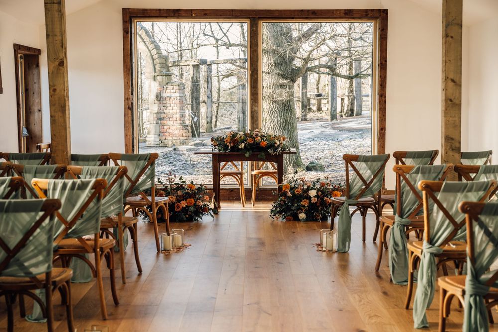 Modern wedding venue setup with cross-back chairs and floral arrangements in natural light.