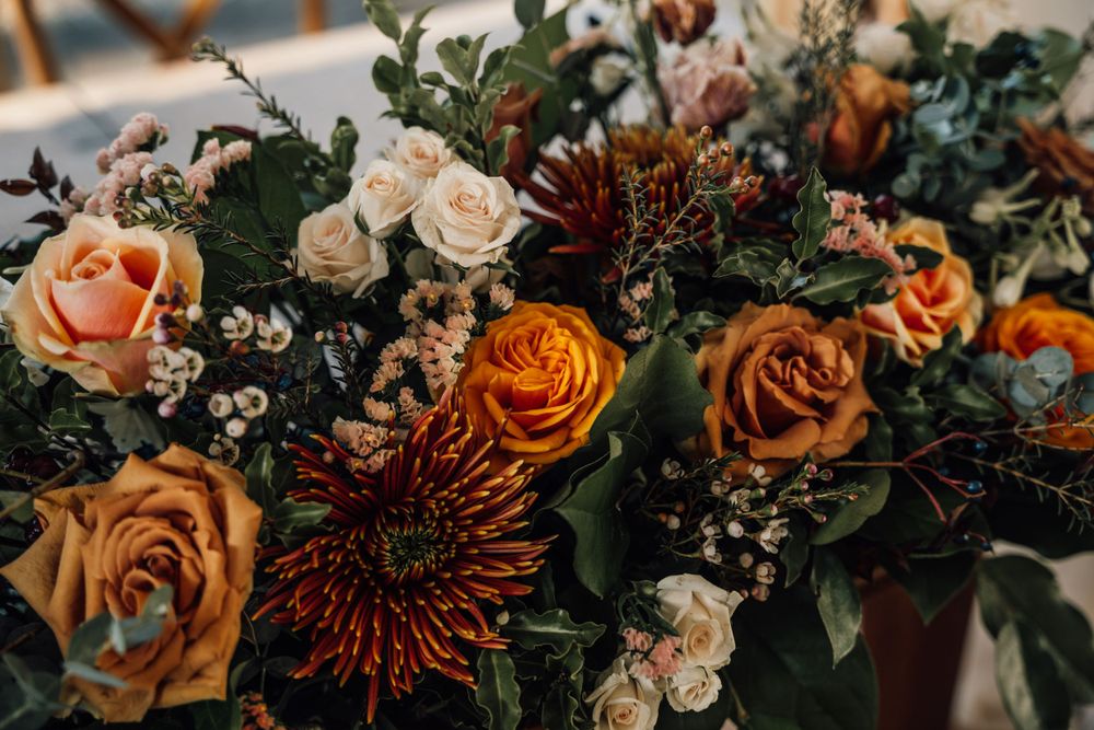 Lush floral arrangement featuring orange roses and burgundy blooms with greenery for wedding decor.