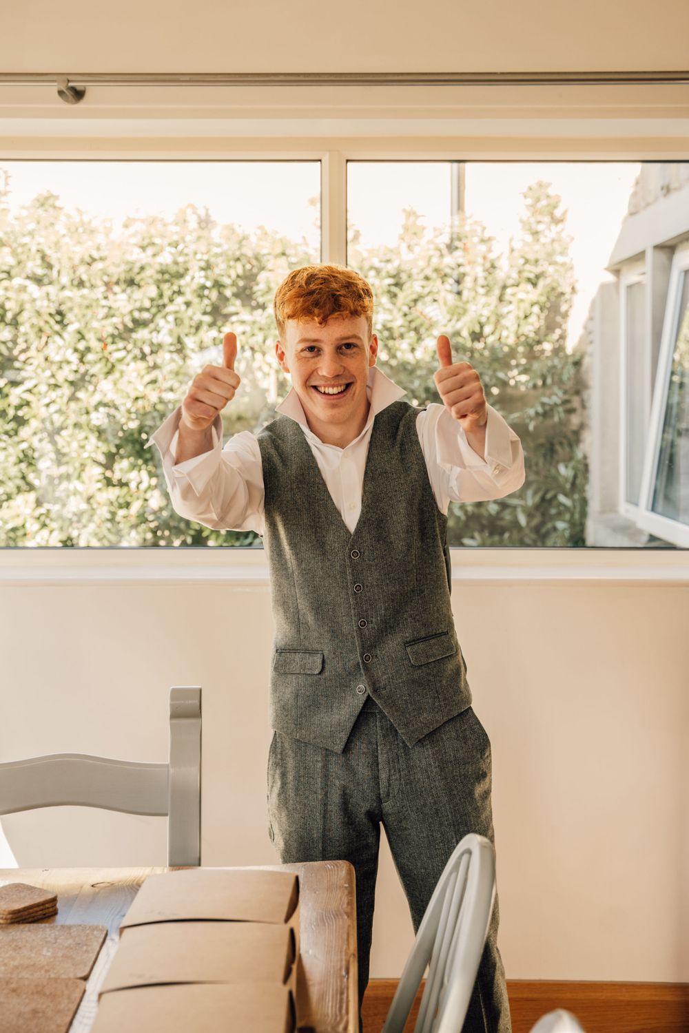 Person in grey vest giving thumbs up gesture in bright sunlit room.