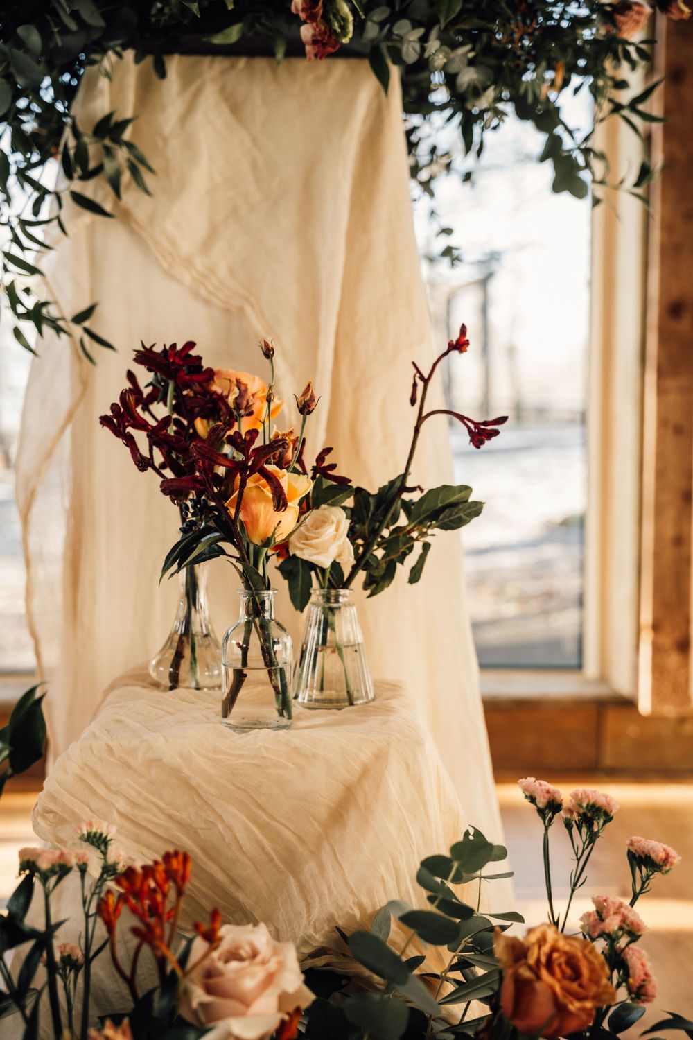 Elegant wedding florals in glass vases against white draping with natural window light.