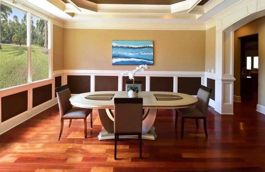 Modern dining room with curved banquette seating, dark wood table, and wall-mounted TV against beige walls with white trim.