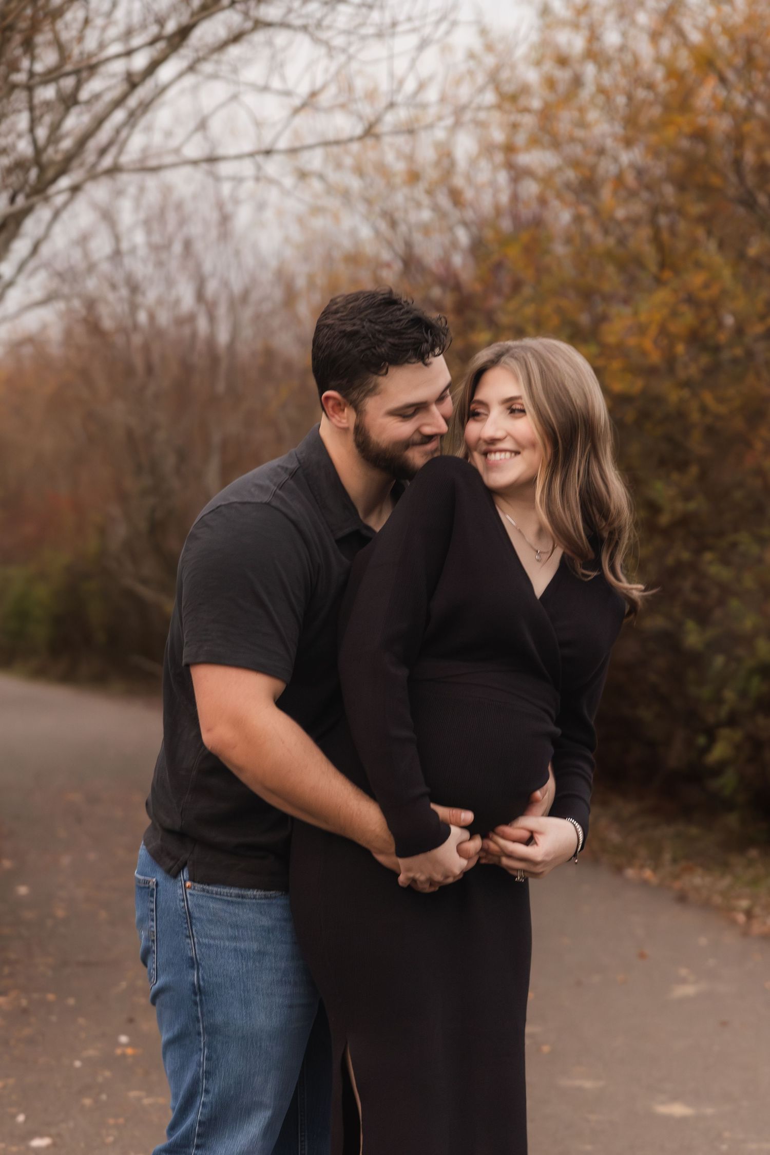 A couple embraces outdoors on an autumn path as they share a tender moment together against fall foliage.