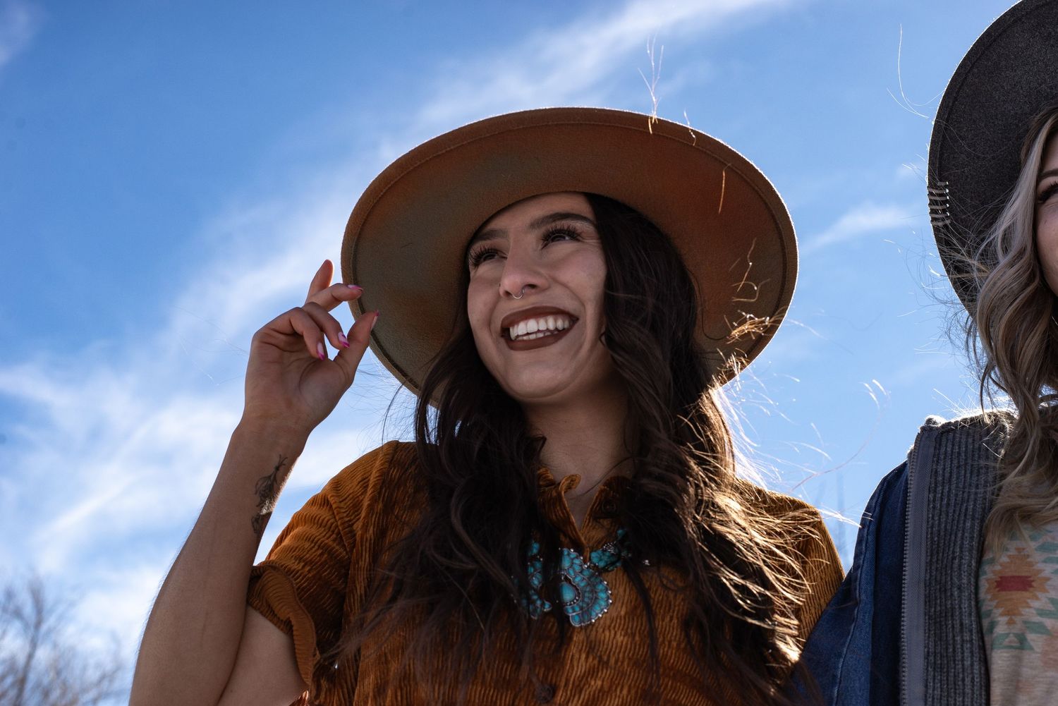 Smiling woman in wide-brim tan hat outdoors on a sunny winter day.