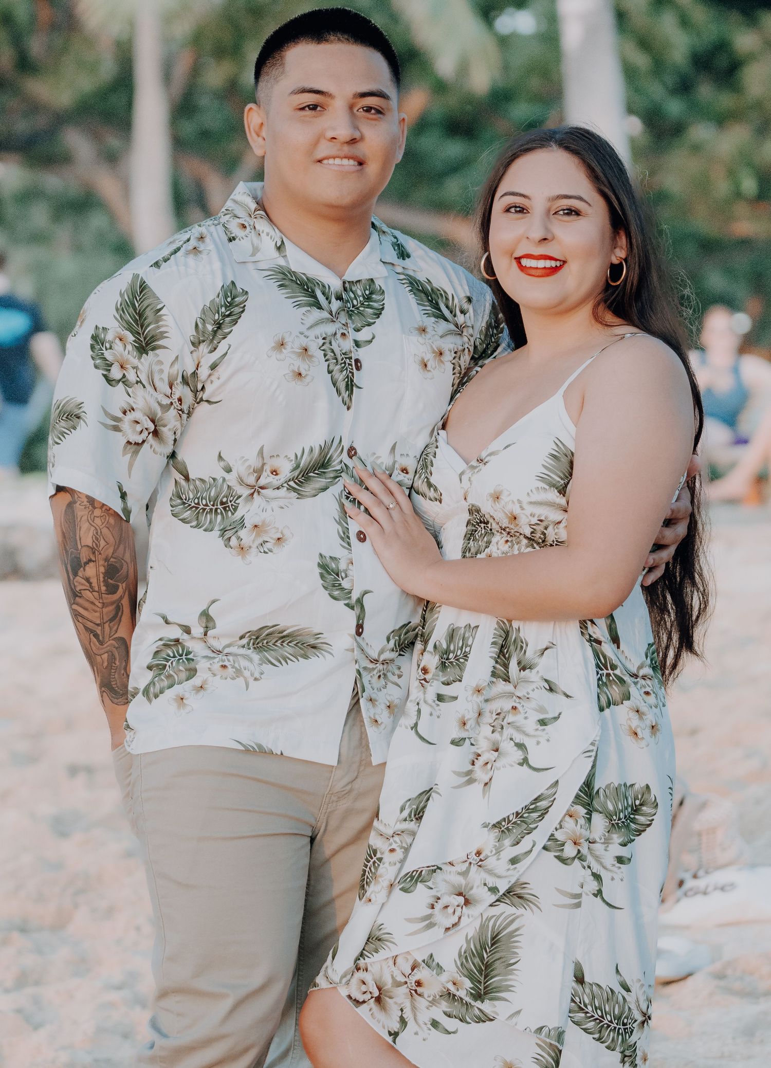 Couple in matching tropical print outfits smiling together on a beach.