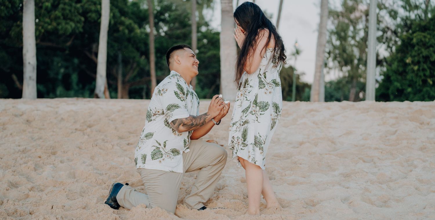 A romantic beach proposal with person kneeling in matching tropical print clothing.